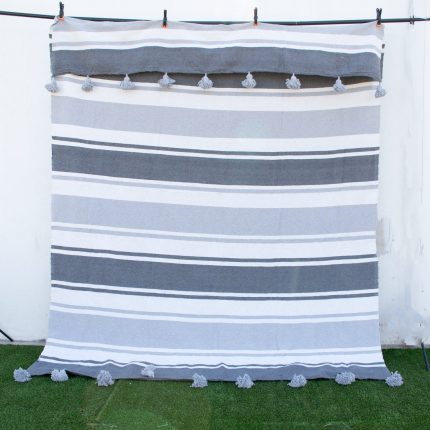 Manta gris con lineas blancas y pompones grises